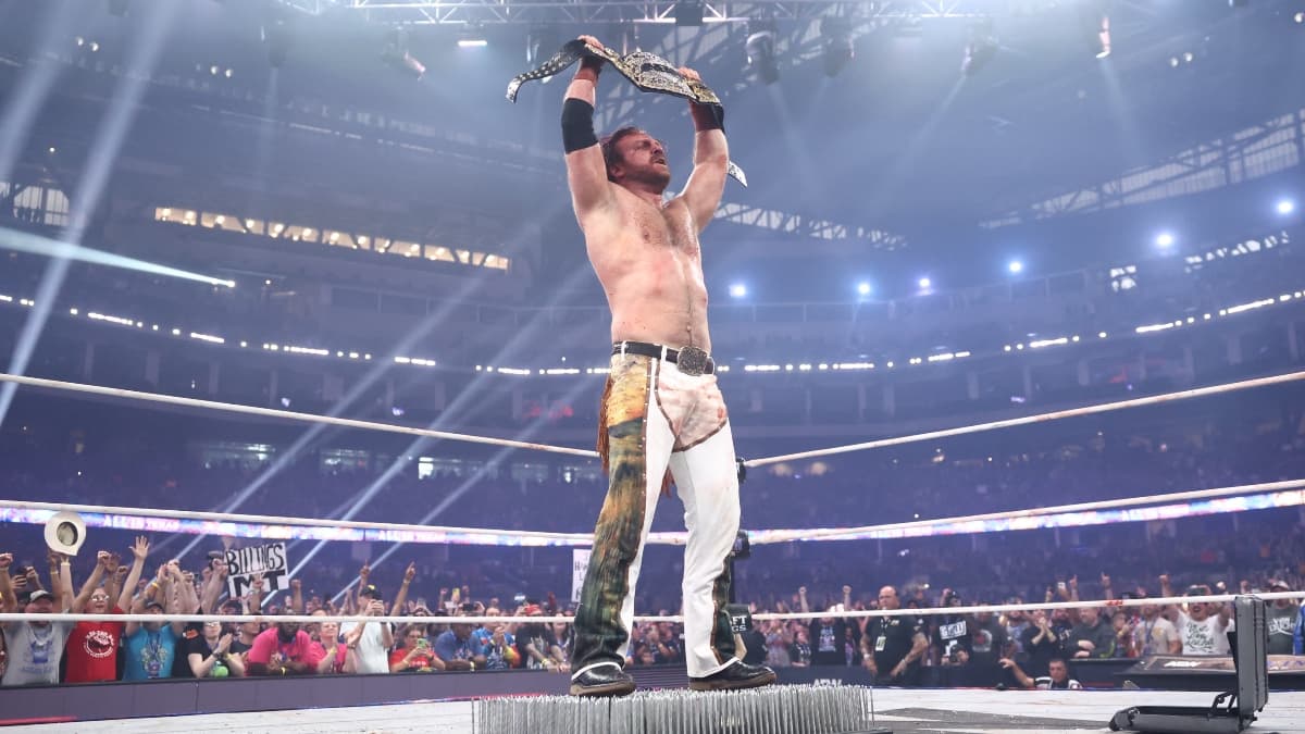 Hangman Page standing on a bed of nails raising the AEW World Title