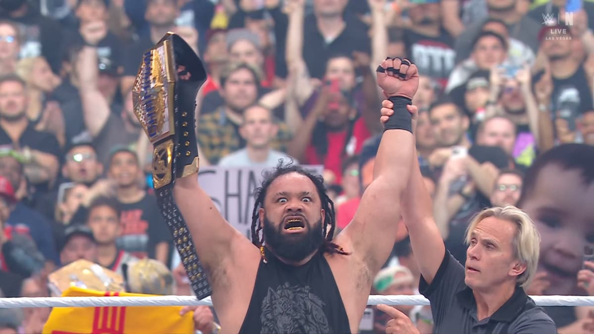 Jacob Fatu holds the US Championship in the air in a WWE ring, the referee raising his arms in victory