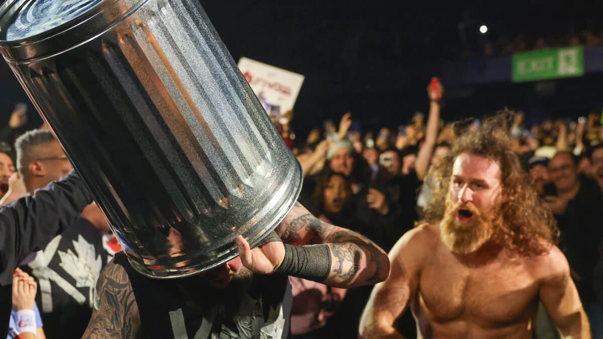 Kevin Owens with a trash can on his head as Sami Zayn walks behind him up some steps inside a WWE arena