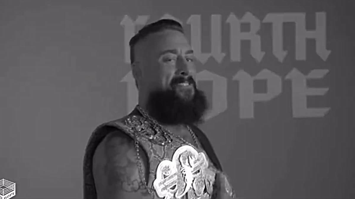 Real1 smirks in black and white with a wrestling championship belt over his shoulder