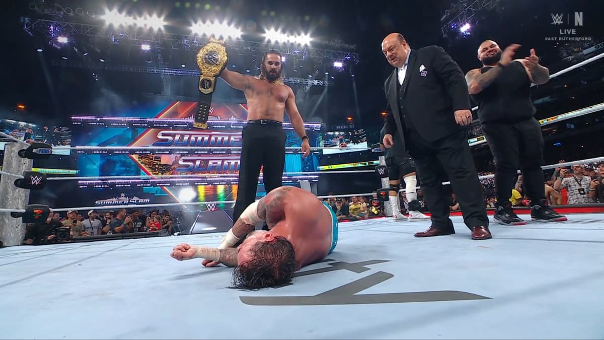 Seth Rollins standing over CM Punk with the World Heavyweight Title alongside Paul Heyman