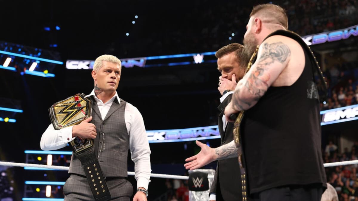 Kevin Owens offering a handshake to Cody Rhodes as Nick Aldis stands between