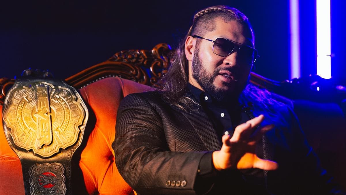 EVIL sitting on a sofa wearing sunglasses and a black suit