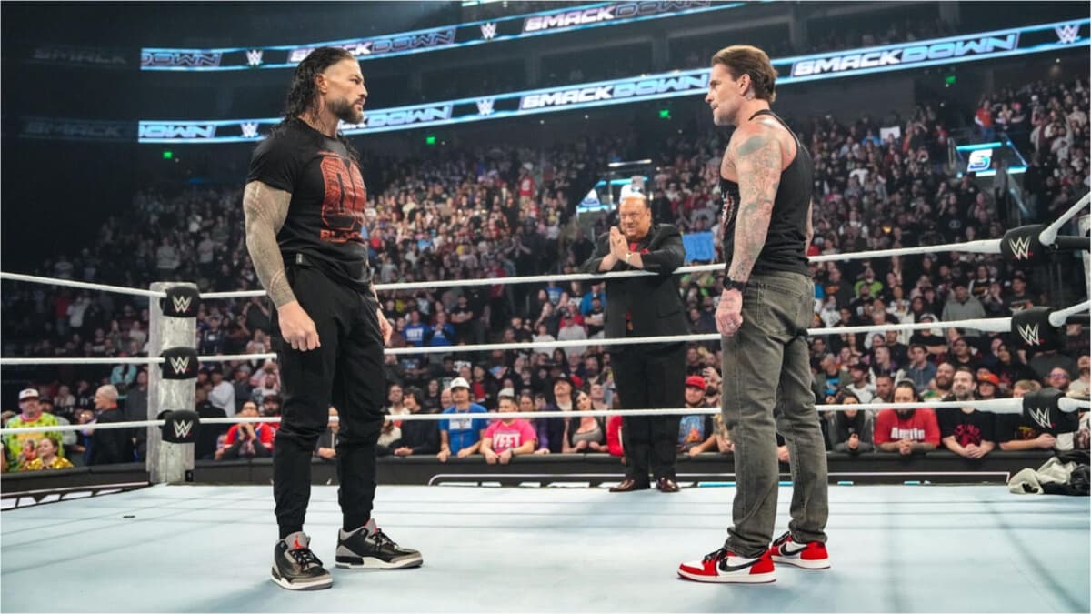 Roman Reigns and CM Punk facing off in the ring whilst Paul Heyman looks on